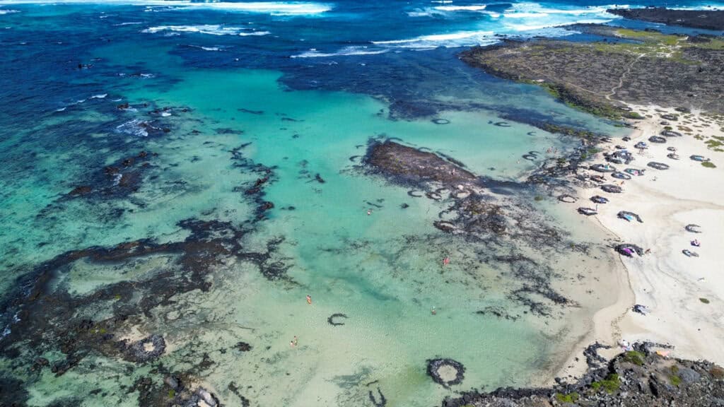 Lagon turquoise et sable blanc de Caletón Blanco entouré de roches volcaniques noires